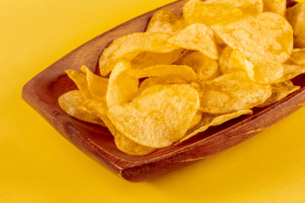 istock Potato chips or crisps in a bowl and scattered on a yellow background 1420996269