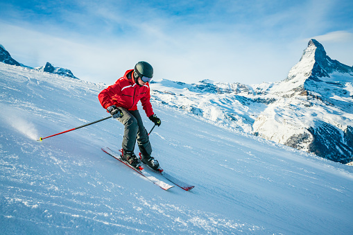 A young aggressive skier on an alpine slope demonstrates an extreme carving skiing style. He is skiing on morning perfectly groomed piste.