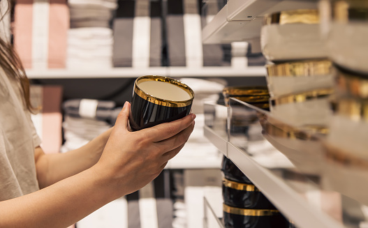 A woman holds a plate in the store against the background of the shelves with dishes, the concept of shopping.