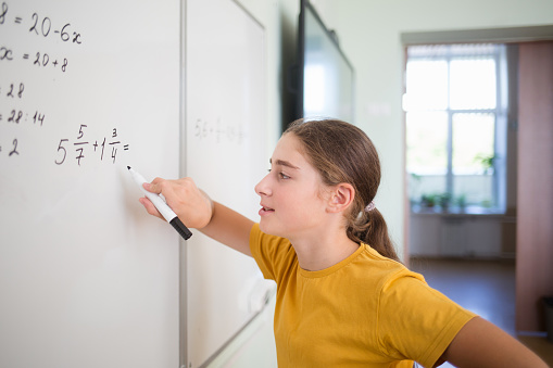 teenager child student solves an example problem with fractions on blackboard in school classroom in math algebra lesson