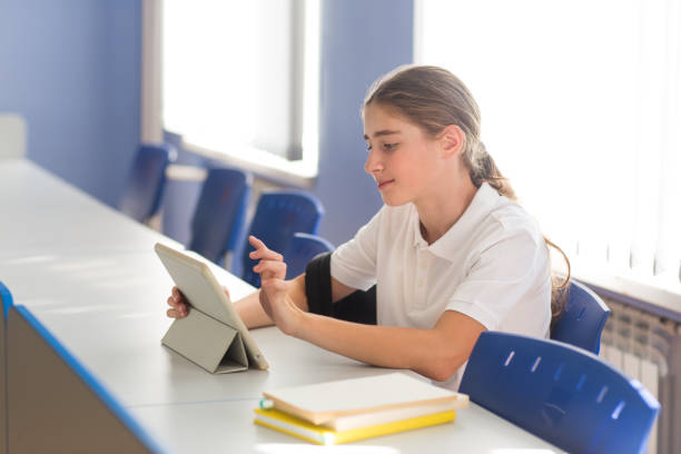student sits at desk in school classroom and studies on tablet.