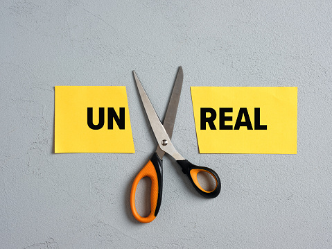 Scissors Cutting off the word unreal and transforming into real. Goal achievement, realistic goals and potential, overcoming difficulties concept.