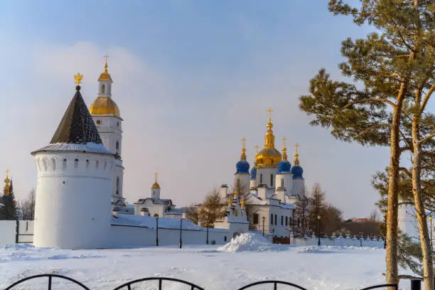 View of the Tobolsk Kremlin (Siberia, Russia) on a frosty winter evening. Numerous old white churches with golden domes contrast with the white snow and blue sky with hints of sunset yellow. Old pine