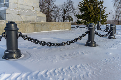 Massive cast iron chains dangling between pillars against a backdrop of white snow. Close-up. Photo taken on a sunny winter day in Siberia (Russia)