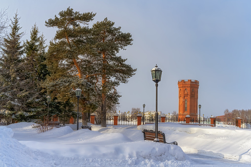 In a winter park with old century-old fir trees. Tall drifts of snow hid the park's wooden benches. a lot of fishnet lanterns. An old brick water tower rises in the distance. Tobolsk (Siberia, Russia)