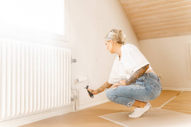 istock Woman painting her walls white with a paint roller 1421001672