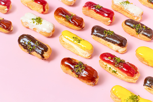Pattern of assortment of eclairs with different topping on pink background. Differentiation and variability concept