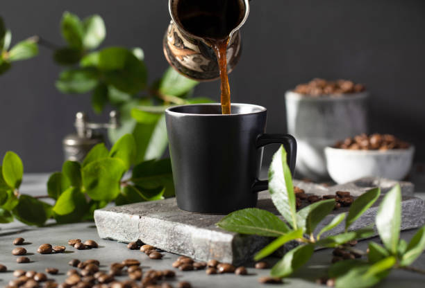 istock Coffee is poured into a black mug from a metal cup on a dark background. 1421013579
