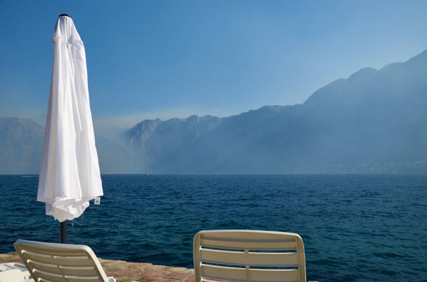Detail of a beach with its white sunbeds and a beach umbrella and with dramatic landscape of blue see and mountains