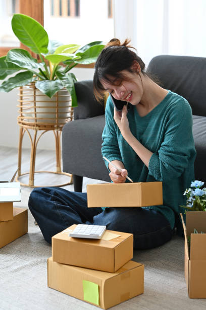 istock Young start up small business owner using smartphone and laptop for receive and checking online purchase shopping order to preparing pack product box. Selling online, Startup small business concept. 1421018197