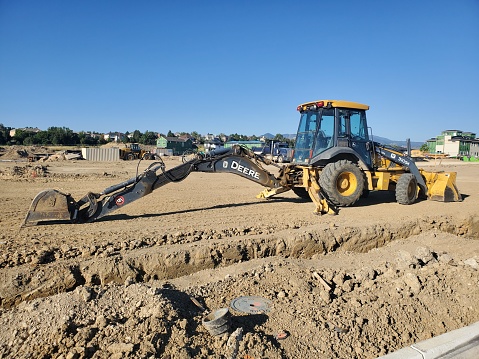 Superior, Colorado, USA-September 4, 2022: John Deere backhoe alongside a pipeline trench at a large construction site.