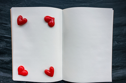 two red paper hearts and open book on wooden table