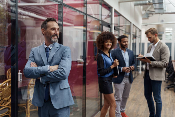 istock Smiling handsome businessman standing in office and looking at side on colleagues background 1421026424