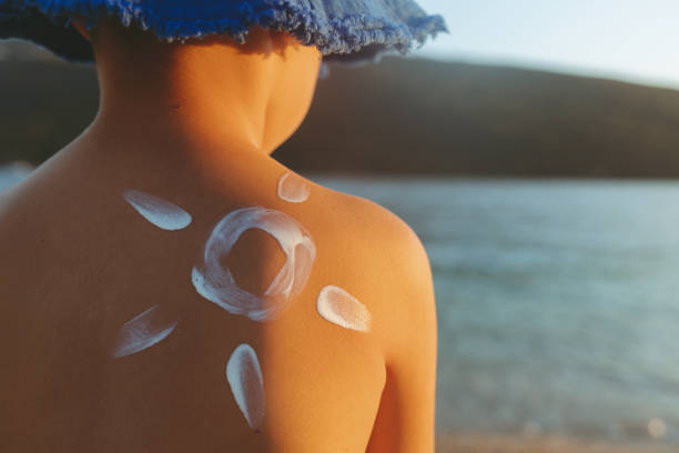 istock Happy child with moisturizer on back at beach wearing blue hat. 1421026570