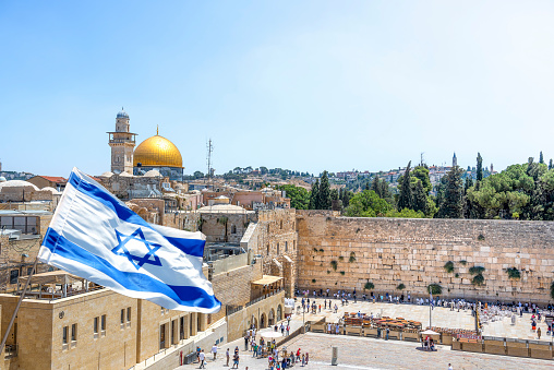 Jerusalem, Israel - September 5, 2022; An Israeli flag blows in the wind from an elevated view of the Western Wall and the Al-Aqsa Mosque in Jerusalem.