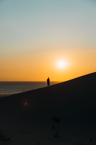 Male explorer walking at the scenic sand dunes with a view of the Mediterranean sea during bright sunset in Patara, Antalya province
