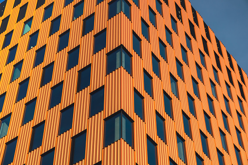 Modern office building exterior with glass facade on clear sky background. Transparent glass wall of office building with orange decoration. Element of facade of modern European building Commercial office buildings. Abstract modern business architecture