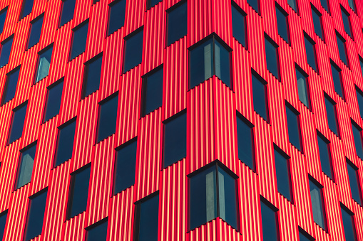 Modern office building exterior with glass facade on clear sky background. Vivid colors Transparent glass wall of office building with red pink decoration. Element of facade of modern European building Commercial office buildings. Abstract modern business architecture