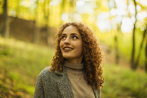 Redhead curly beautiful girl in coat in autumn forest. Pretty woman enjoying vacation. Visit local attractions. Girl laughing in nature. Feel happiness. Charming smile. Happy lady