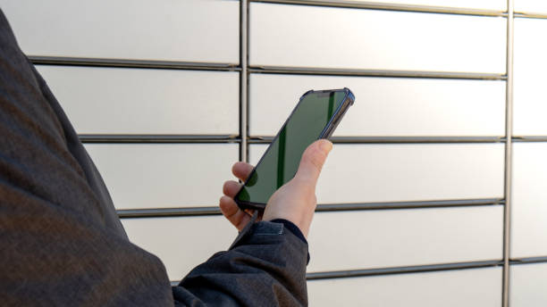 Female hand holding mobile phone next to Parcel locker Collecting parcel from shopping locker. Woman Skans QR Code on Mobile phone Self-service Locker Cell with Bar code Reader Modern Shipping and Delivery Concept with Contactless Automated Postal Box mujer sosteniendo la mano del teléfono móvil junto al armario de paquetes recogiendo el paquete de la taquilla de compras. mujer skans código qr en teléfono móvil autoservicio locker cell con lector de código de barras envío moderno y entrega sin co