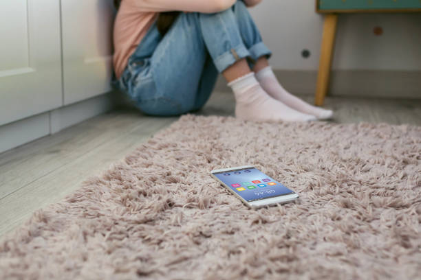 teléfono móvil tirado en el suelo con una niña triste irreconocible sentada detrás - carpet caucasian domestic room home interior fotografías e imágenes de stock