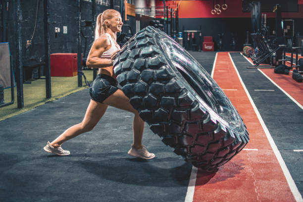 femme blonde en forme qui retourne un pneu lourd au gymnase. - throwing wheel photos et images de collection