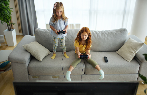 Closeup of two sisters playing video games in the living room.