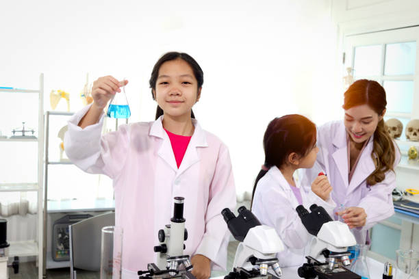istock Students and teacher in lab coat have fun together while learn science experiment in laboratory. Young adorable Asian scientist kid showing blue flask with teacher and classmate as blur background, little children students study research at school lab. Sc 1421040571