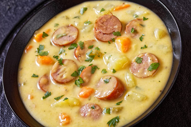 Kartoffelsuppe, German potato soup with sausages in black bowl on  concrete table, close-up