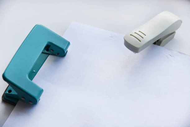 A white stapler and a green hole punch on a white background. Stationery on a white background.