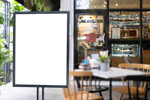 Shop sign on an easel mockup. White blank signboard stand near the entrance to the coffee shop, mock up, cafeteria blurred background can inserting the text of the customer.