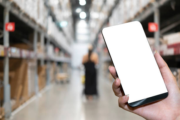 istock Warehouse with a hand holding an empty smartphone. blurred industrial warehouse with goods and products. logistics, business 1421048291