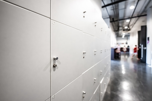 Large gray locker with each locker closed located beside corridors inside building are dimly lit.