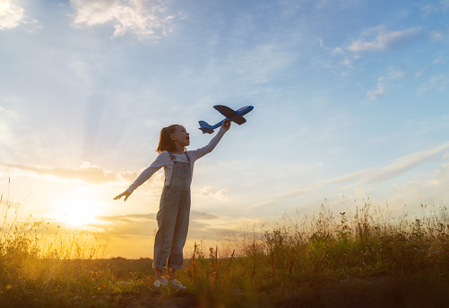 Happy kid with toy plane is playing at sunset.