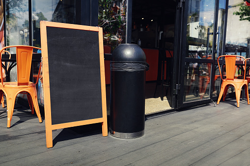 Blank chalkboard in wooden frame stands on terrace of street cafe or restaurant outside