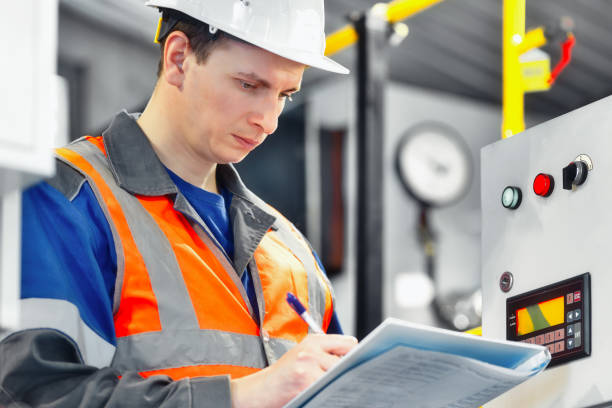 istock Young engineer in helmet and vest stands inside compression station and makes entry in journal. 1421054587