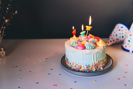Colorful birthday cake with sprinkles and burning star shaped candles on a dark wall background. Festive birthday celebration, party. Selective focus, copy space