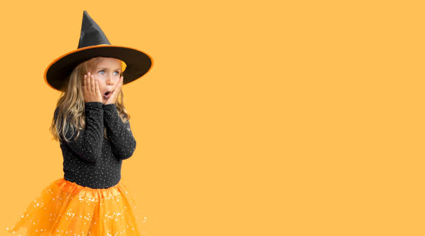 surprise excitée petite fille portant un chapeau de sorcière costume halloween isolé fond de studio jaune. vente saisonnière et rabais. shopping attentif. promouvoir les biens. bannière, espace de copie pour le texte, maquette - surprise child little girls shock photos et images de collection