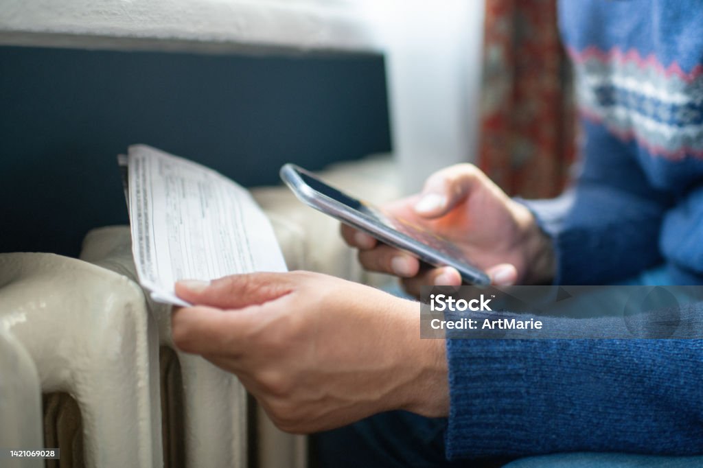 Man trying to warm up near a heater Man's cold hands in warm sweater on radiator in winter. Energy crisis concept. Financial Bill Stock Photo