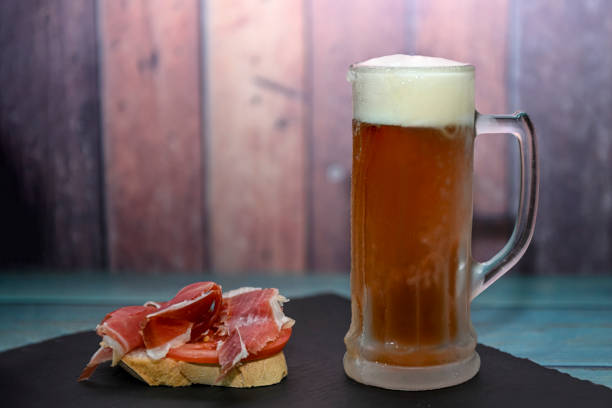 istock Ice cold mug of beer with a Jamon appetizer, on a wooden table. 1421069745