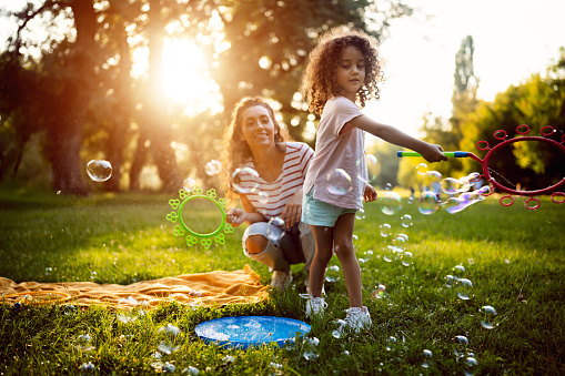 Caucasian mother and daughter, playing in the nature, while making soap bubbles with bubble wand