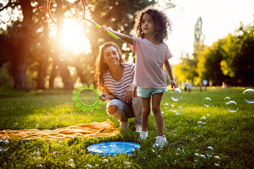 Caucasian mother and daughter, playing in the nature, while making soap bubbles with bubble wand