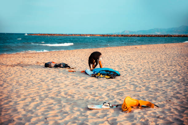 Man on a beach preparing his kite on sand beach for kitesurfing on sea waves