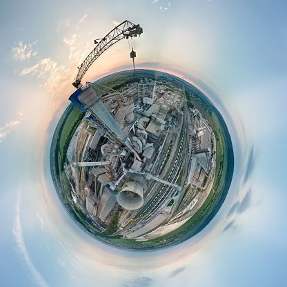 Aerial view from high altitude of little planet earth with cement factory high concrete structure and tower crane at industrial production area in evening. Manufacture and global industry concept.