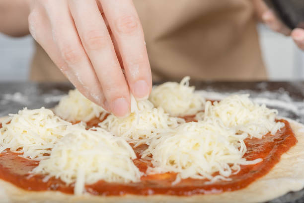 A woman in an apron prepares Margherita pizza in her kitchen.