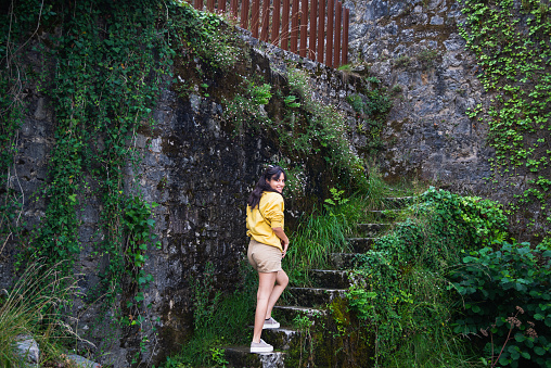 Young woman in yellow sweater, climbing an old stone staircase, located on the river bank.