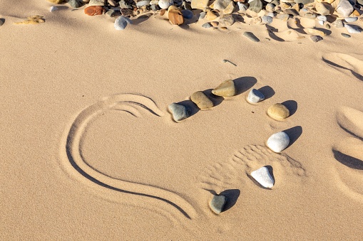 Heart shape created from half pebbles and half line drawn in the sand