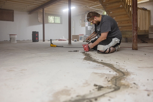 Worker sealing basement floor cracks to protect house from mold.