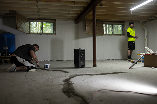 Two workers waterproofing basement floor with hydraulic cement.
