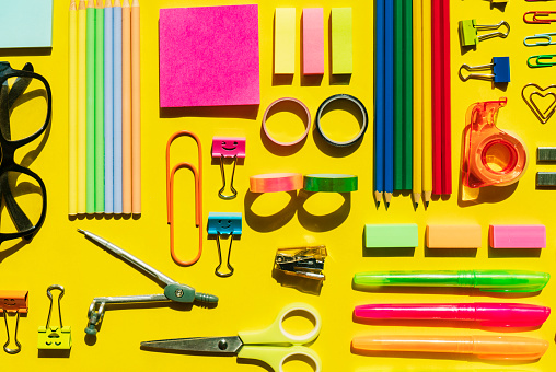 Office and school supplies arranged on yellow background